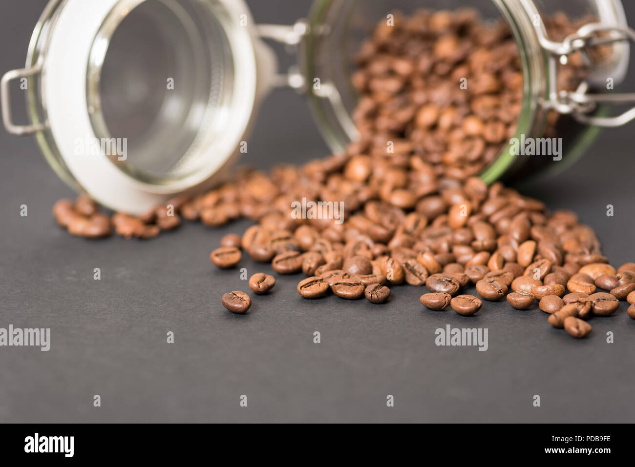 Pot de rangement alimentaire verre couché sur côté avec café en grains tomber sur la surface noire Banque D'Images