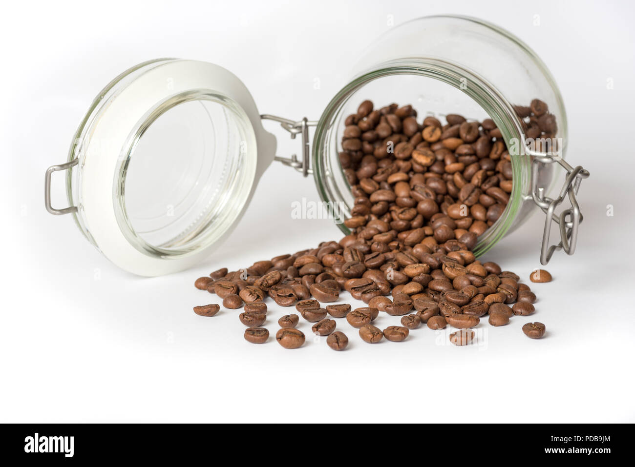 Pot de rangement alimentaire verre couché sur côté avec café en grains tomber sur la surface blanche Banque D'Images