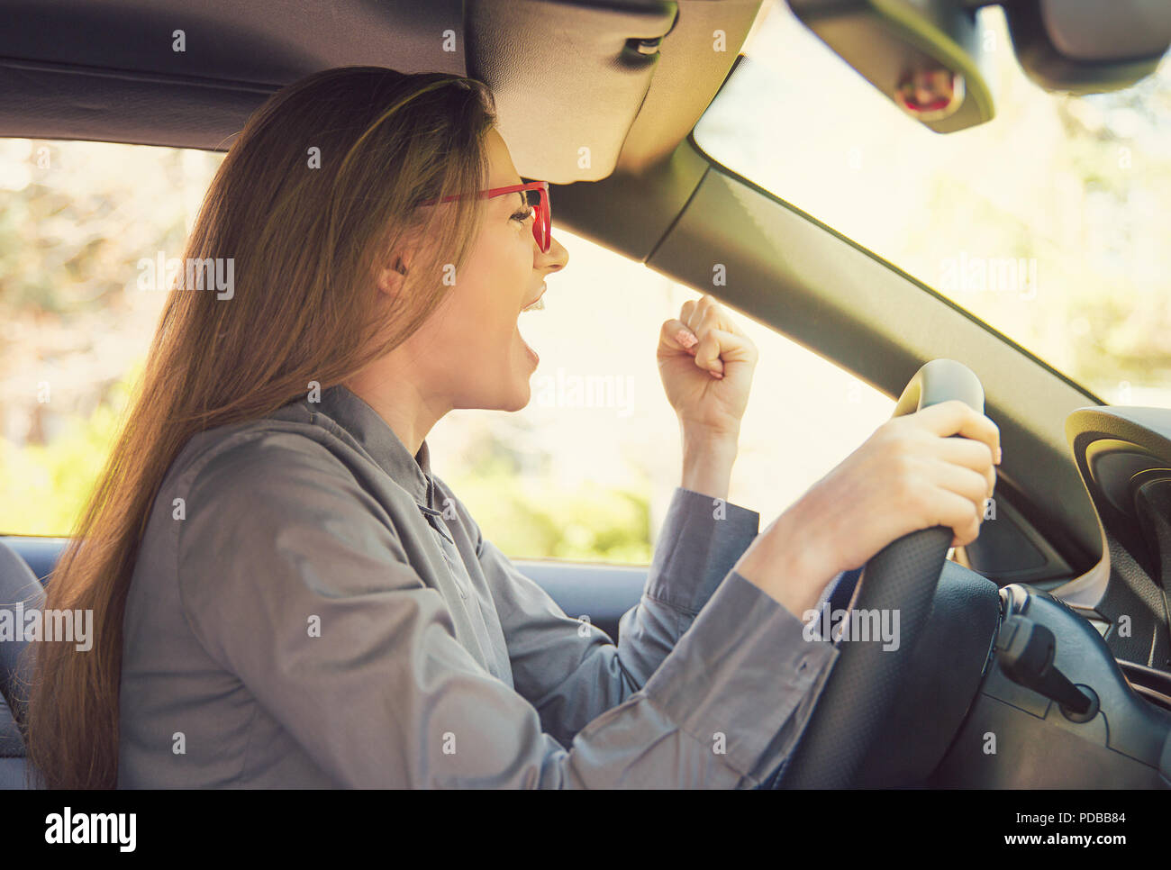 Vue latérale du jeune femme en voiture conduite lunettes et gesticulant émotionnellement dans la colère à la voiture pendant les heures de pointe Banque D'Images