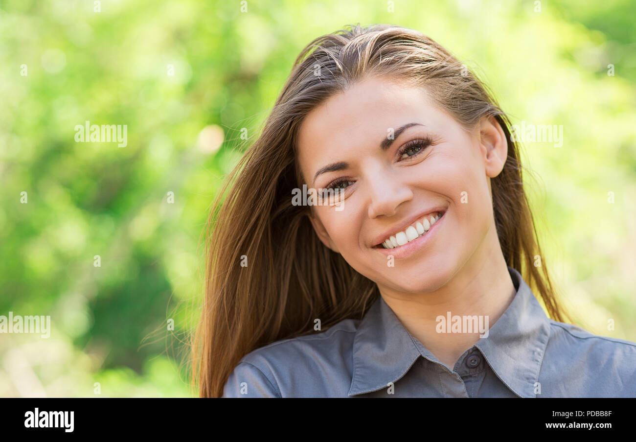 Pretty young woman in casual shirt smiling at camera heureusement debout sur fond vert en parc d'été Banque D'Images