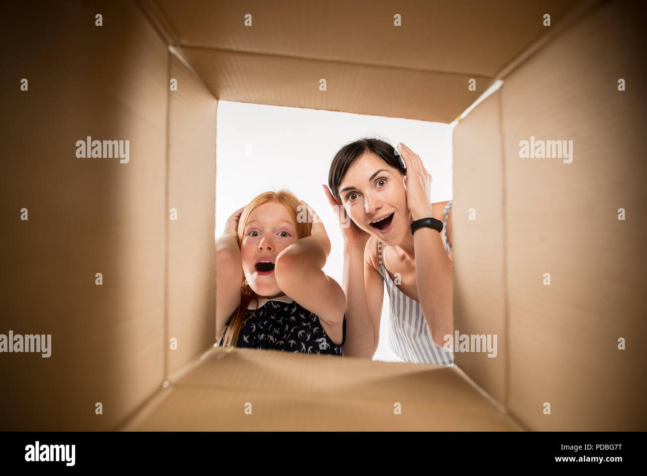 L'étonné maman et fille du déballage, l'ouverture de la boîte en carton et à l'intérieur. L'emballage, la livraison, la surprise, la vie cadeaux concept. Les émotions humaines et les expressions faciales concepts Banque D'Images