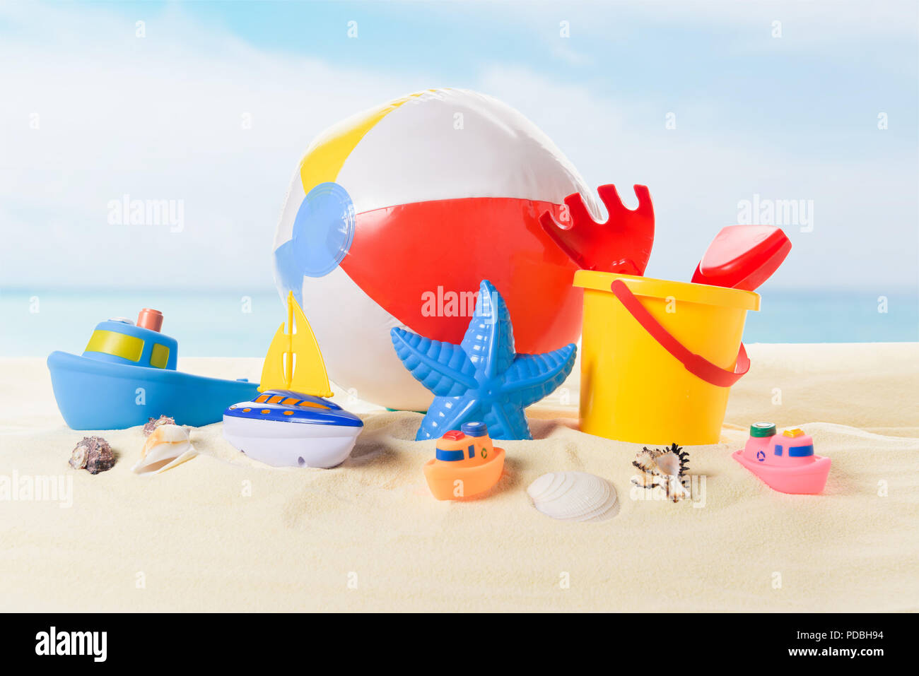 Ballon de plage et du godet avec des jouets dans le sable sur fond de ciel bleu Banque D'Images