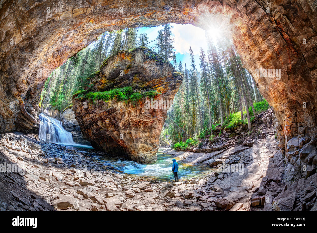 Randonneur se tient dans la crainte d'une chute d'eau et la roche calcaire à une cachette secrète dans la région de Johnston Canyon du parc national de Banff, avec du soleil dans le jardin luxuriant de rupture Banque D'Images