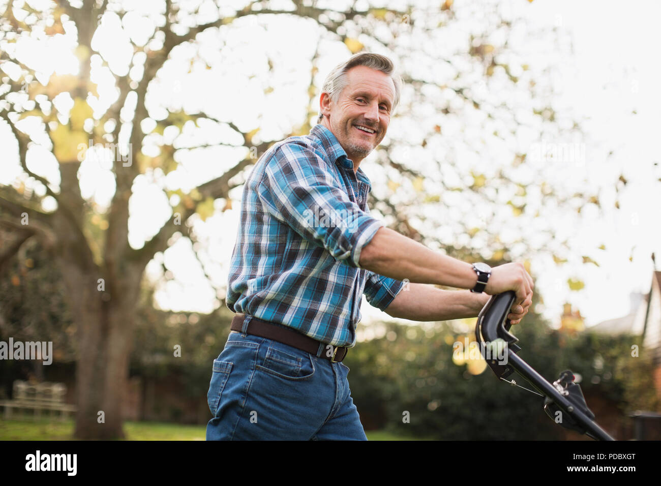 Portrait of smiling senior man mowing lawn Banque D'Images