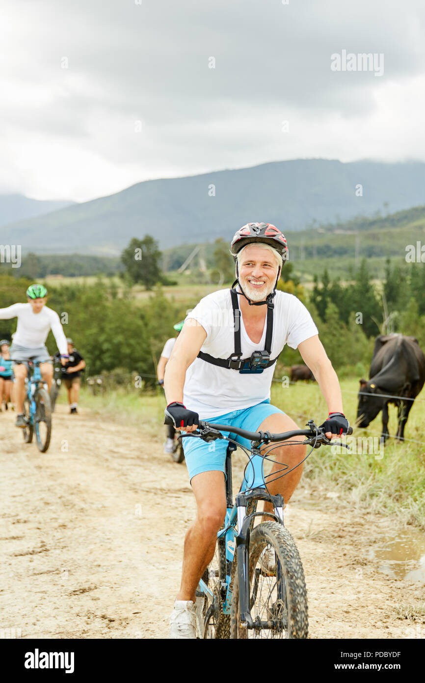 Souriant, confiant mature man mountain biking on rural road Banque D'Images