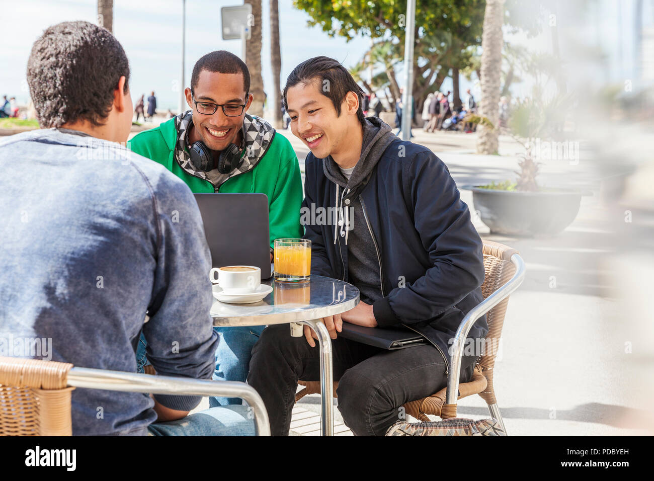 Amis de sexe masculin à l'aide d'ordinateur portable au café avec terrasse ensoleillée Banque D'Images