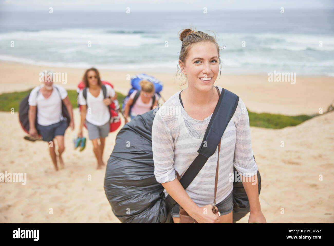 Portrait souriant, confiant femme transportant un sac à dos parachute parapente on beach Banque D'Images