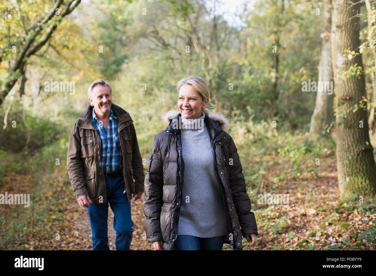 Smiling mature couple walking in sunny autumn woods Banque D'Images