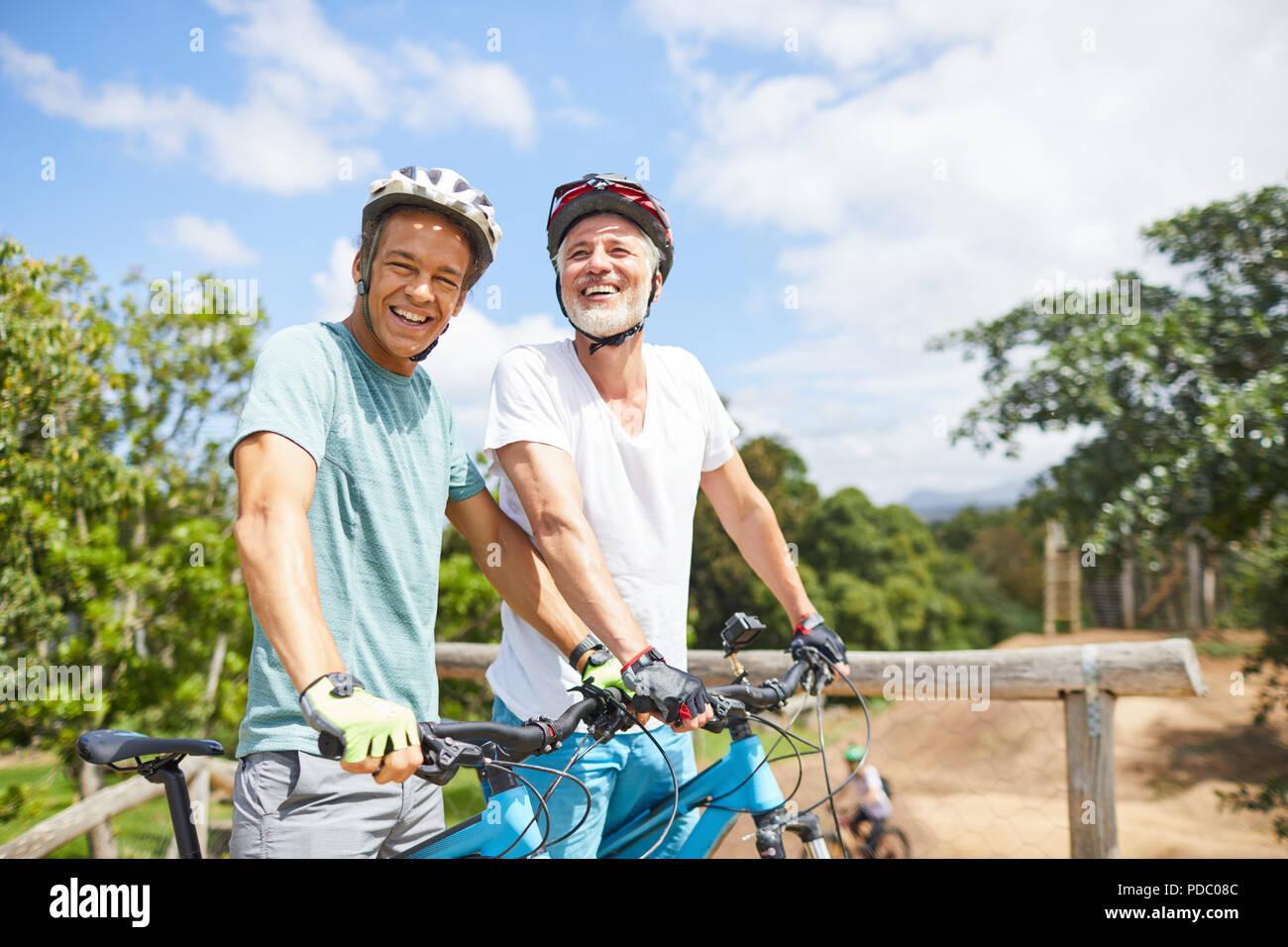 Portrait confiant père et fils randonnée cycliste sur piste ensoleillée Banque D'Images