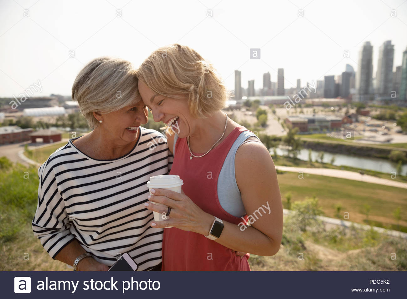 Mère et fille affectueuse avec café en parc urbain ensoleillé Banque D'Images