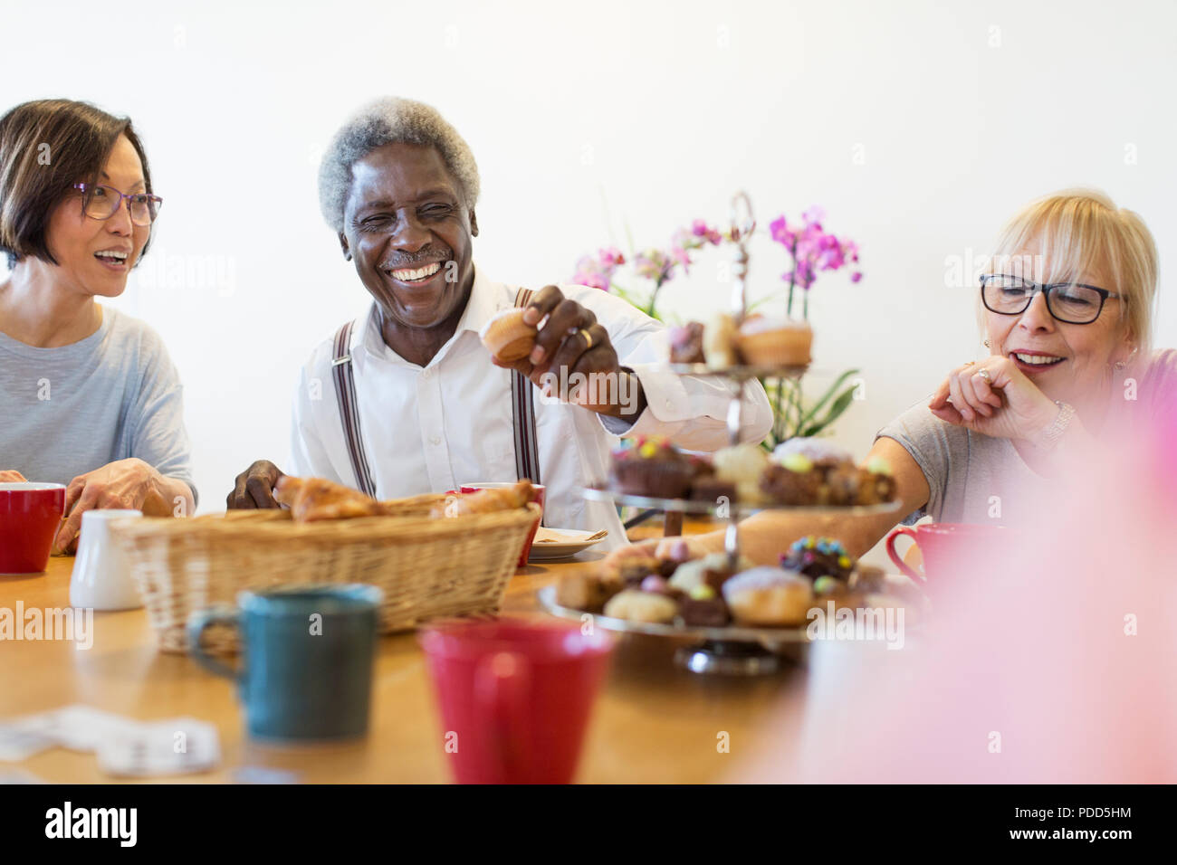 Happy friends enjoying afternoon tea desserts dans community centre Banque D'Images
