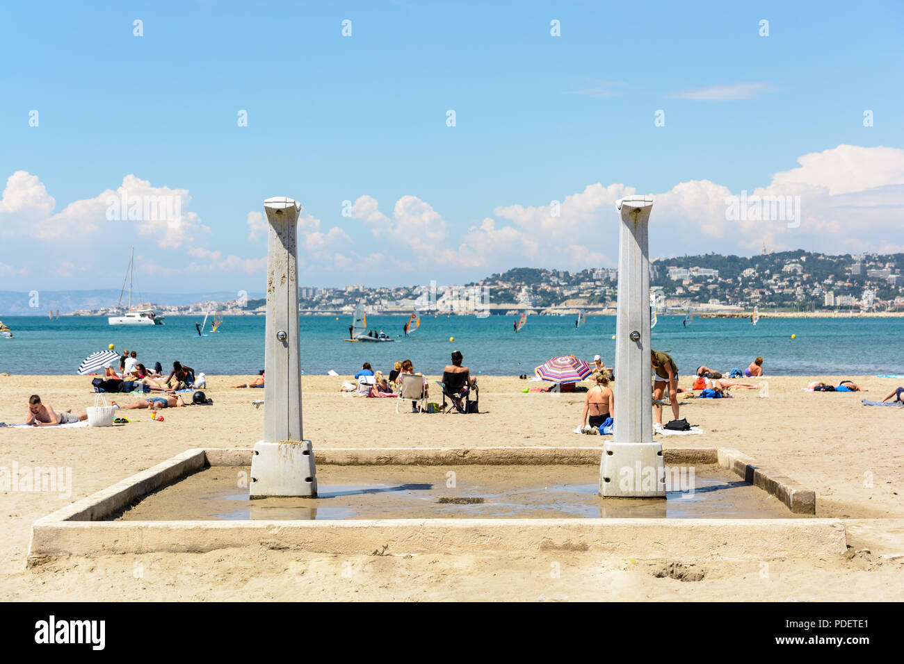 Les douches de plage de plage de la Pointe Rouge à Marseille, France, avec des gens de soleil et planche à voile à l'arrière-plan par une journée de printemps ensoleillée et chaude. Banque D'Images