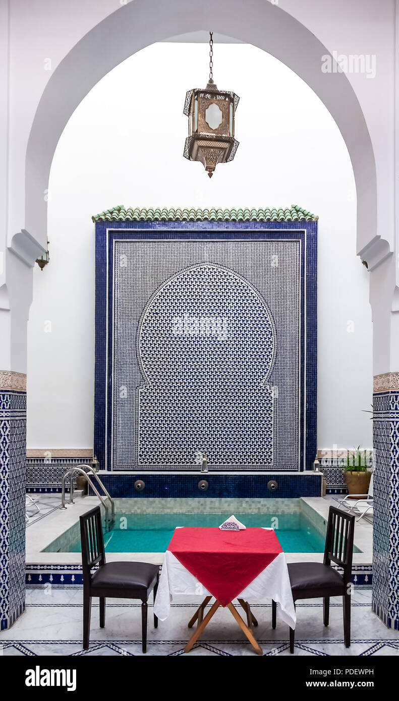 Fes, Maroc - 11 mai 2013 : riad marocain cour intérieure décorée avec des mosaïques et des arcades mauresques mis en place avec table et chaises avec une piscine i Banque D'Images