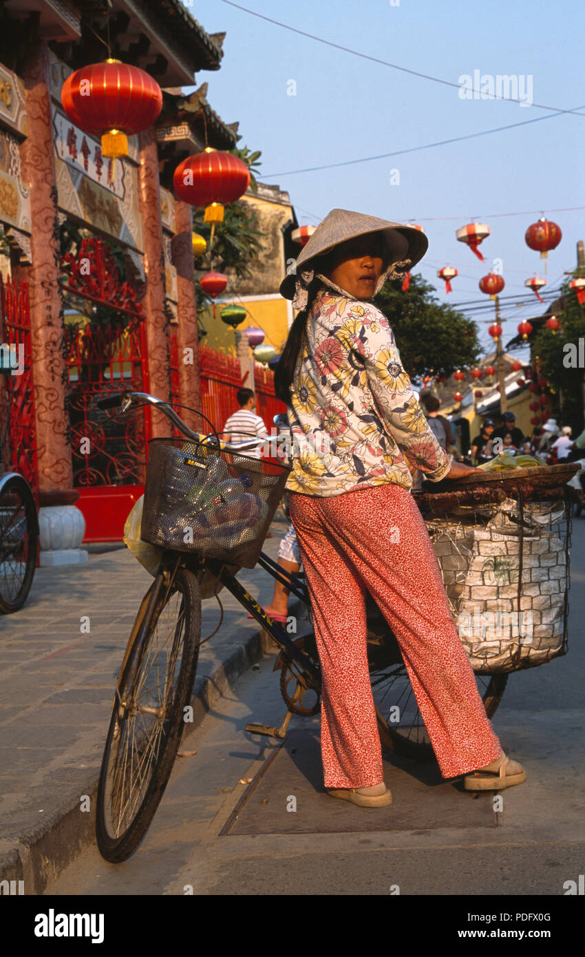 Femme portant un pantalon et chemise à fleurs avec coolie hat standing with bicycle in street à Hoi An, Vietnam pour un usage éditorial uniquement Banque D'Images