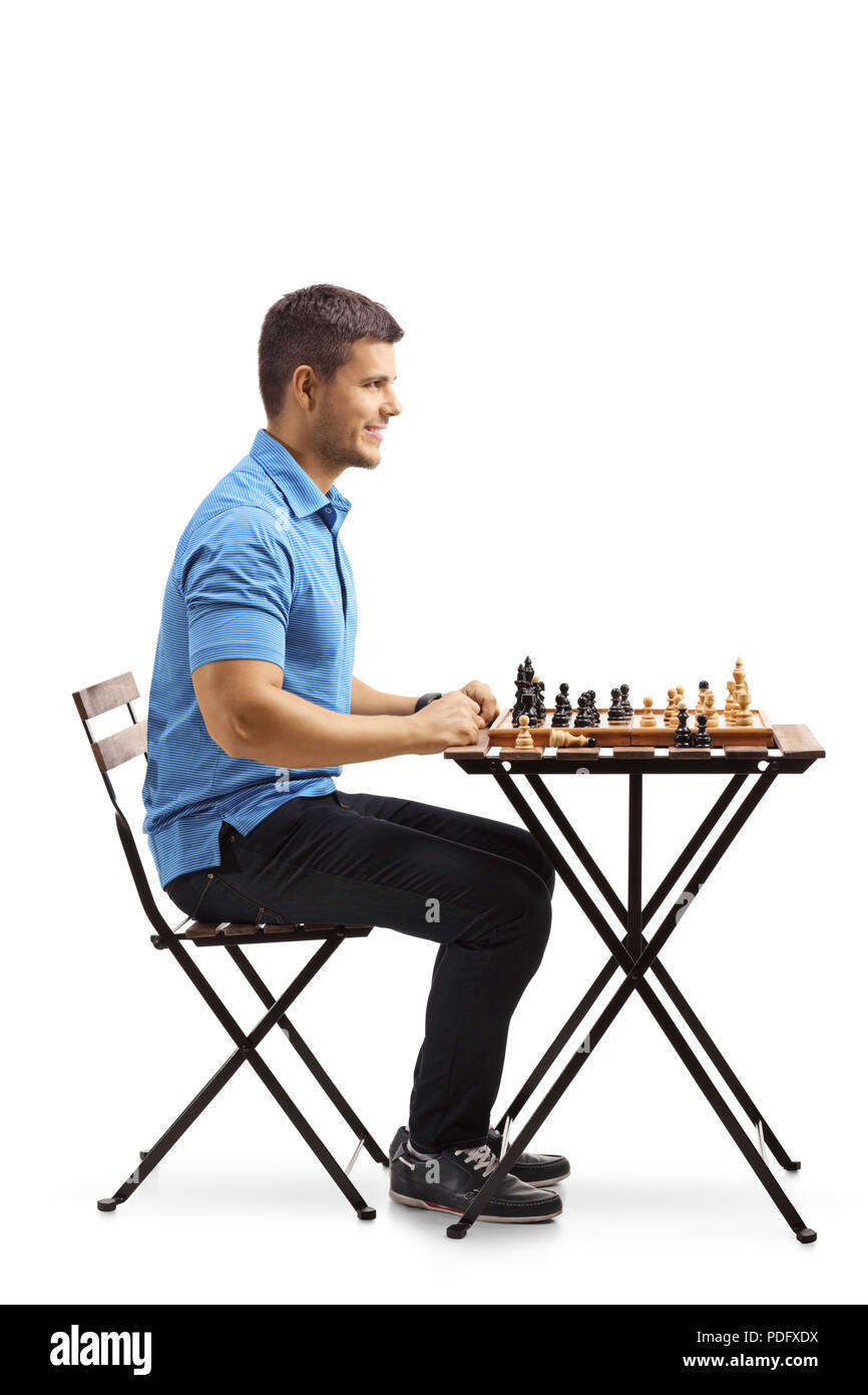 Jeune homme assis à une table jouant aux échecs isolé sur fond blanc Banque D'Images