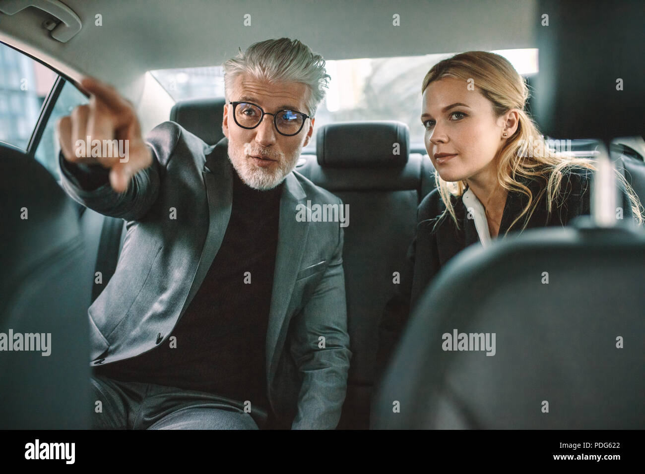 Deux hommes d'affaires voyageant en voiture avec l'homme en pointant à l'écart. Senior businessman montrant quelque chose d'intéressant à femme lors d'un voyage par un taxi. Banque D'Images