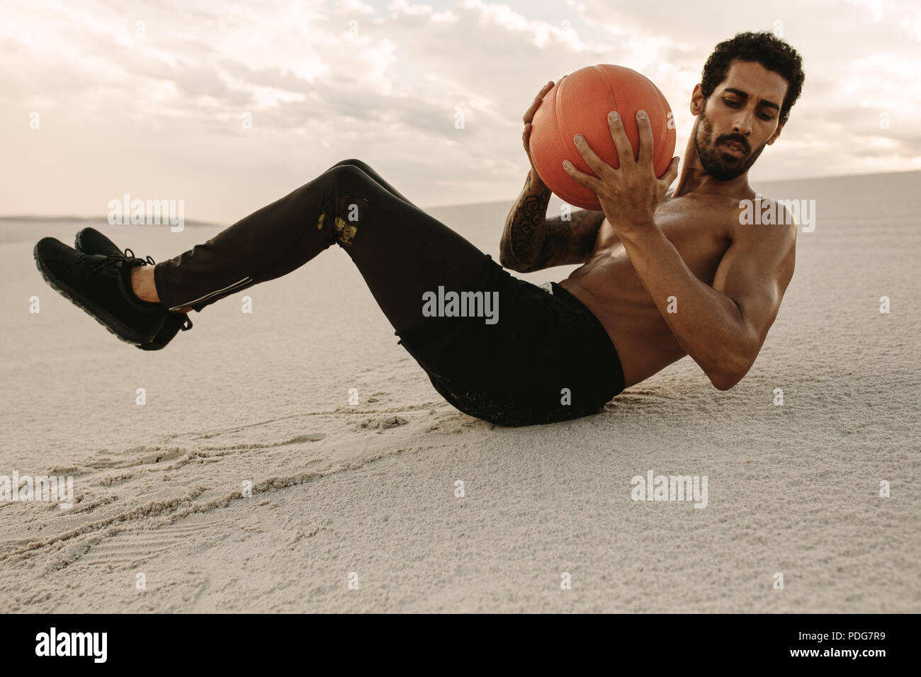 Jeune homme fort de faire un ballon d'entraînement sur les dunes de sable. À l'aide de l'athlète un ballon pour la formation de remise en forme dans le desert. Banque D'Images