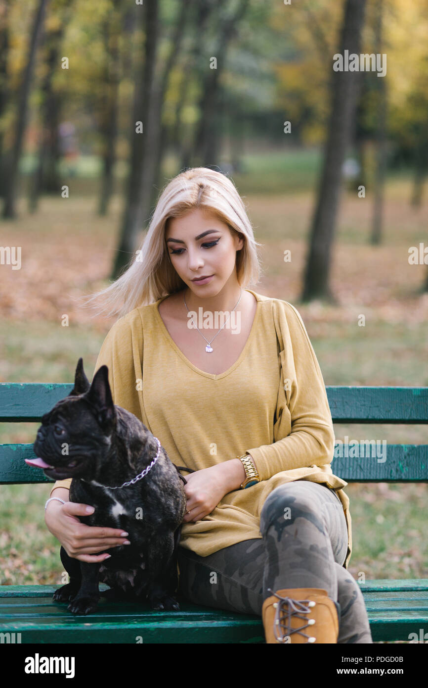 Belle et heureuse femme assis sur un banc de parc avec son adorable bouledogue français. Banque D'Images