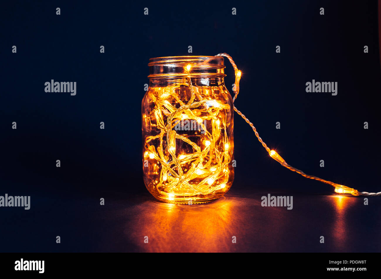 Fée de Noël lumières dans un pot Mason, brillants dans le noir, sur un fond bleu. Banque D'Images Fée de Noël lumières dans un pot Mason, brillants dans le noir, sur un fond bleu. Banque D'Images