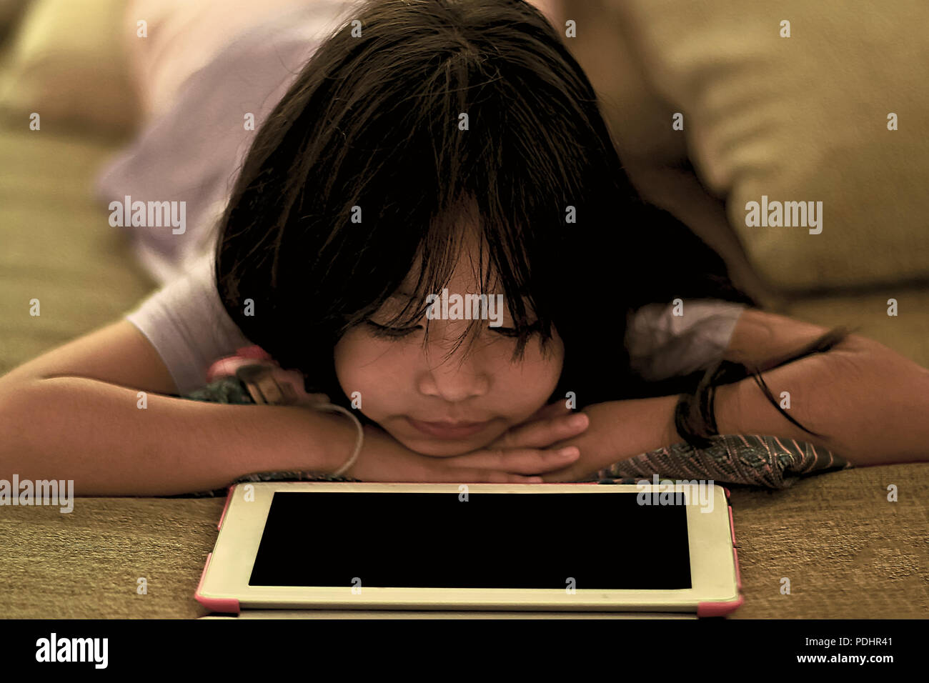 Cute young girl couchée sur le canapé à la recherche d'écran de tablette numérique Banque D'Images