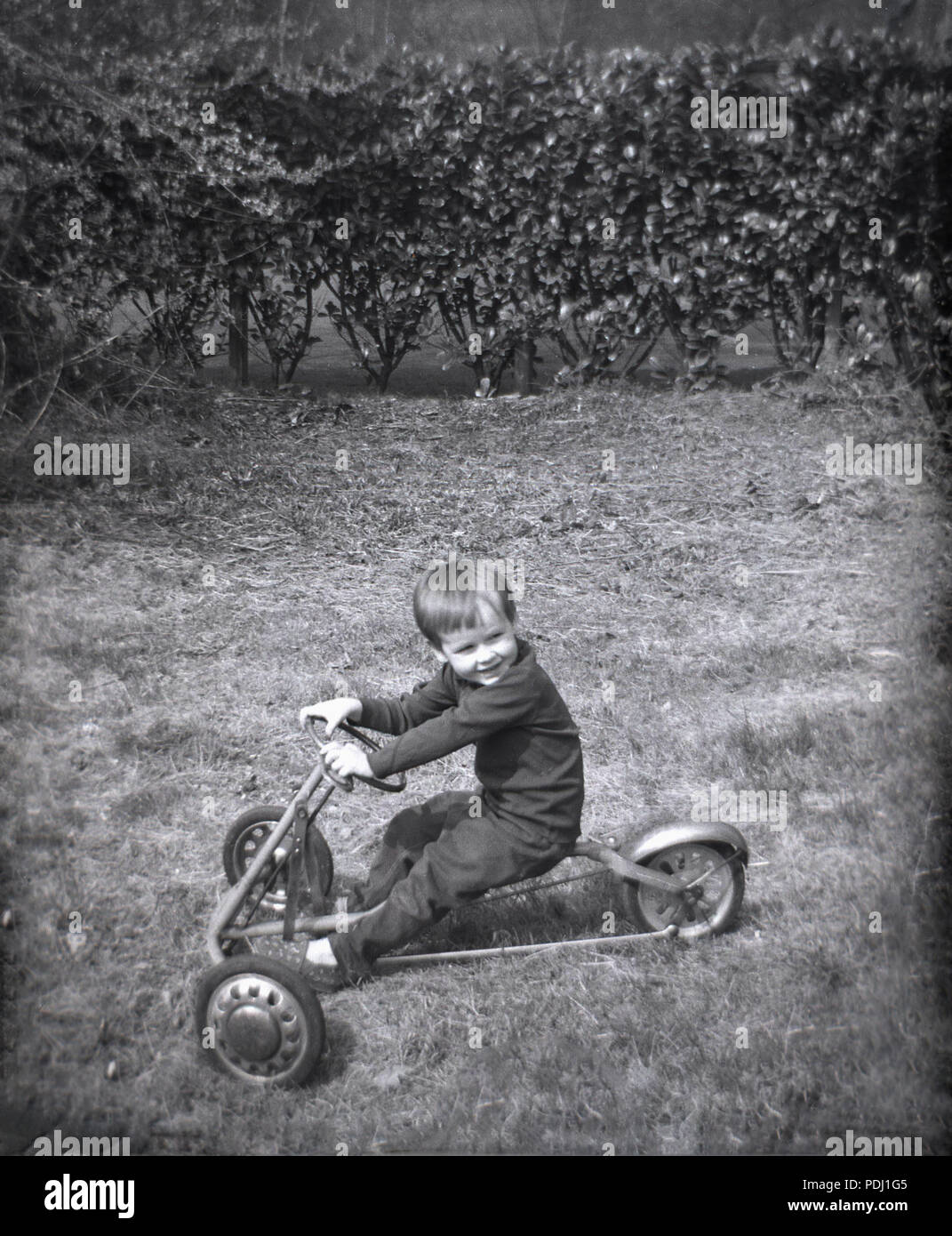 Années 1960, historiques, jeune garçon assis sur un trois-roues métal pédales toy-kart en dehors de l'herbe dans un jardin, England, UK. Banque D'Images