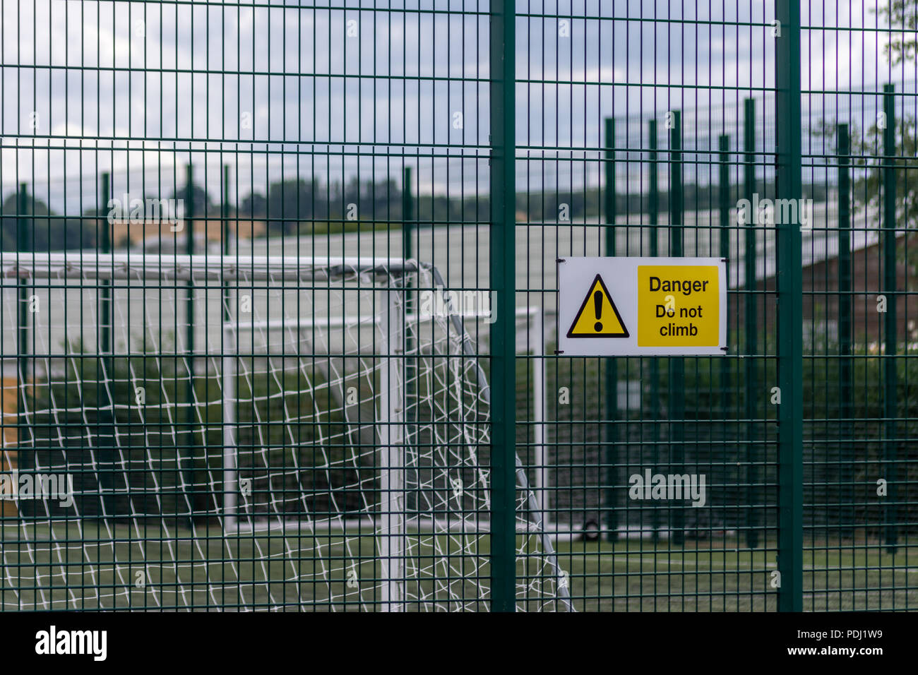 Inscrivez-vous prévenir d'un danger sur une grille métallique rigide clôture avec poteaux de but de football visible derrière le grillage Banque D'Images