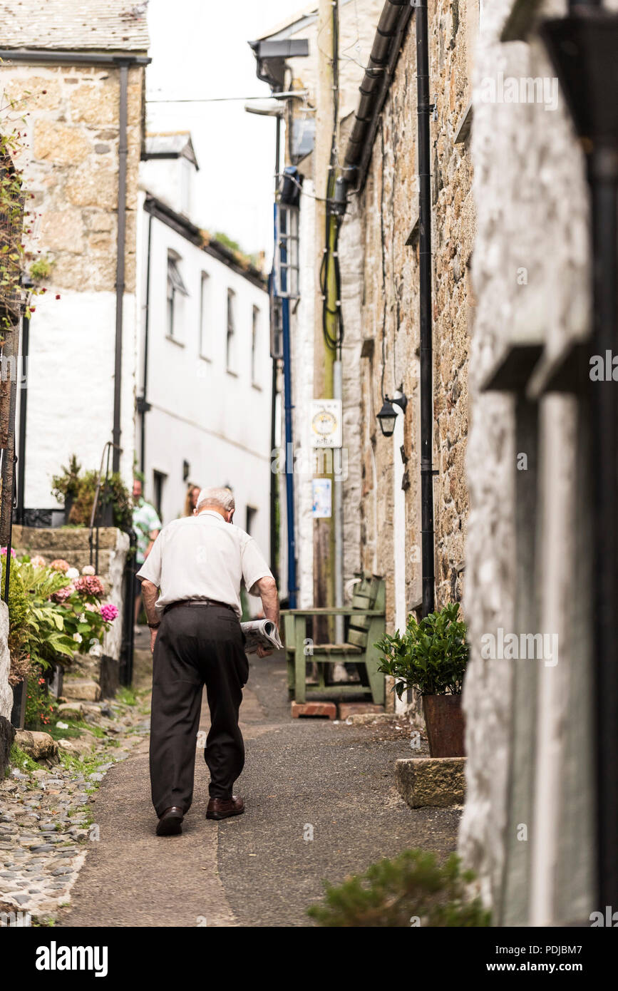 A mature man walking up Duck Street dans le village de Mousehole Cornish historique. Banque D'Images