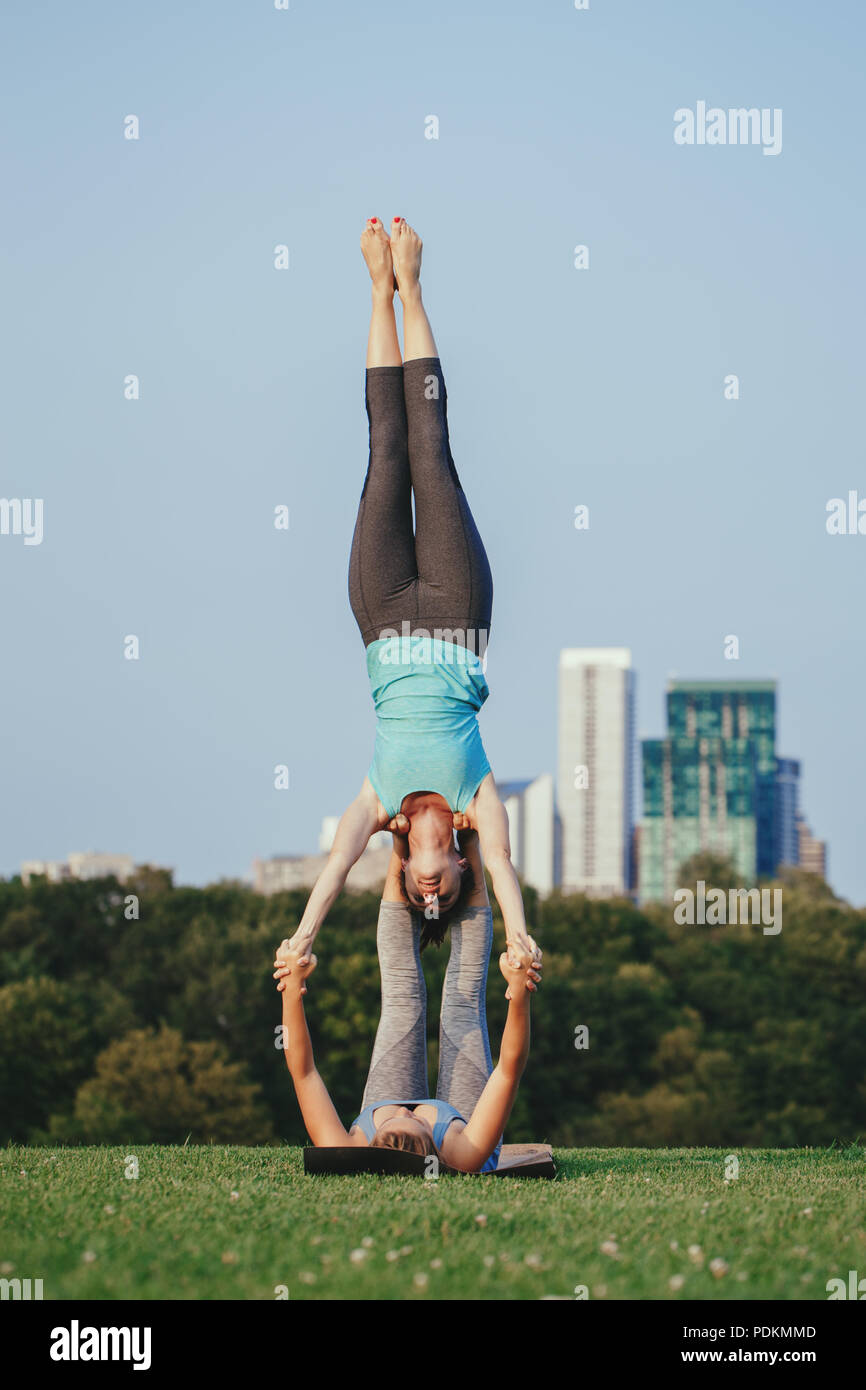 Deux jeunes femmes de race blanche épaule étoiles faisant yogi yoga acro stand. Les femmes qui s'étend à l'extérieur du parc d'entraînement au coucher du soleil. Mode de vie sain Banque D'Images