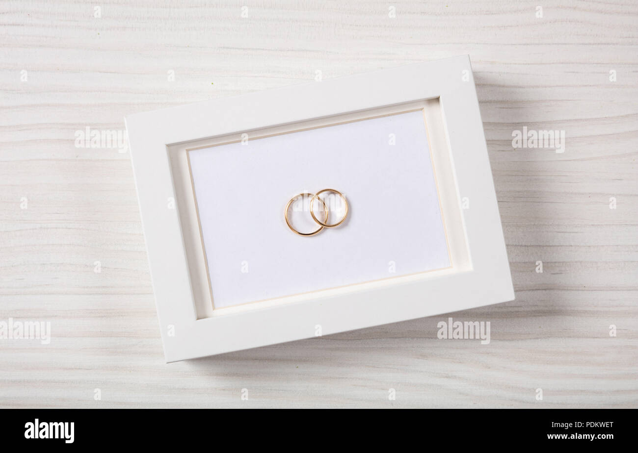 Amour et Mariage concept. Les anneaux de mariage en or blanc sur un fond noir cadre photo, vue d'en haut, isolé sur un fond de bois blanc. Banque D'Images