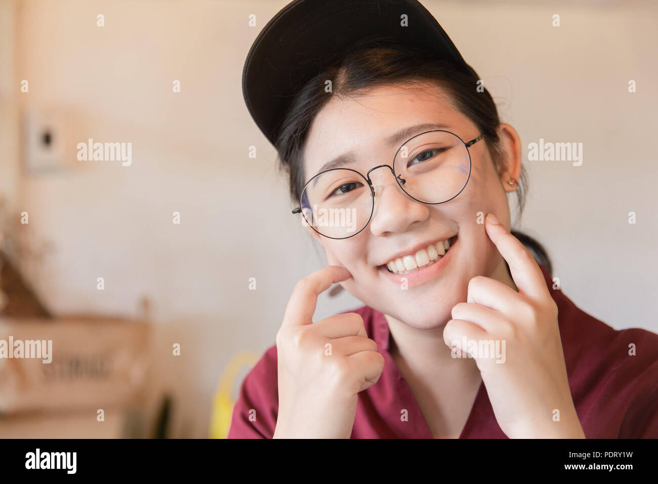 Plump Chubby teen mignon sourire dent blanche jeune étudiante asiatique avec des lunettes et un chapeau doigts joue with copy space Banque D'Images