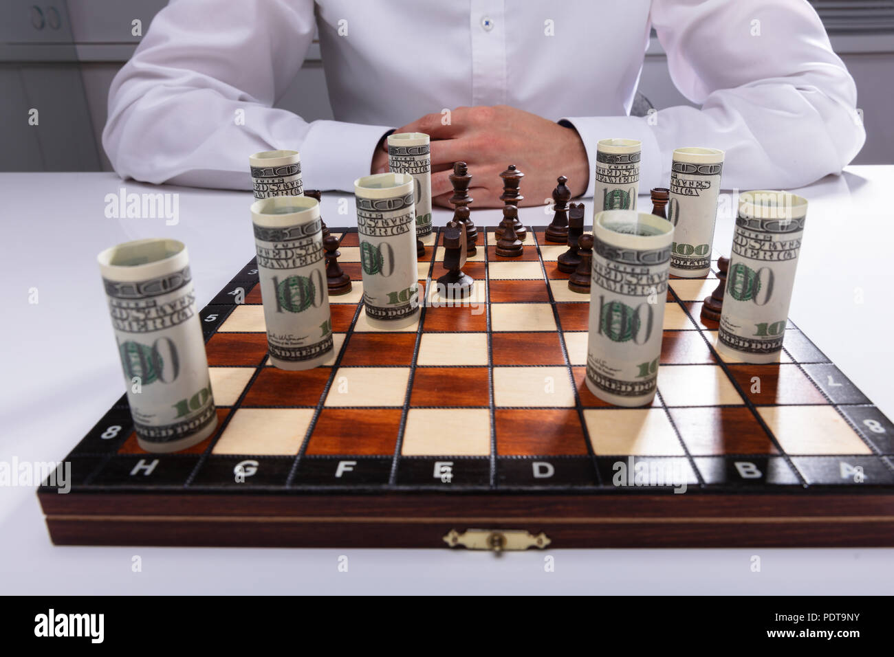 Businessman Jouer aux échecs avec des pièces et billets de banque américains enroulé Banque D'Images