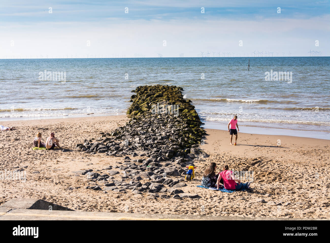 Les gens se détendre par la roche à épi plage centrale, Prestatyn, Nord du Pays de Galles, Royaume-Uni., au cours de l'été de canicule 2018. Banque D'Images