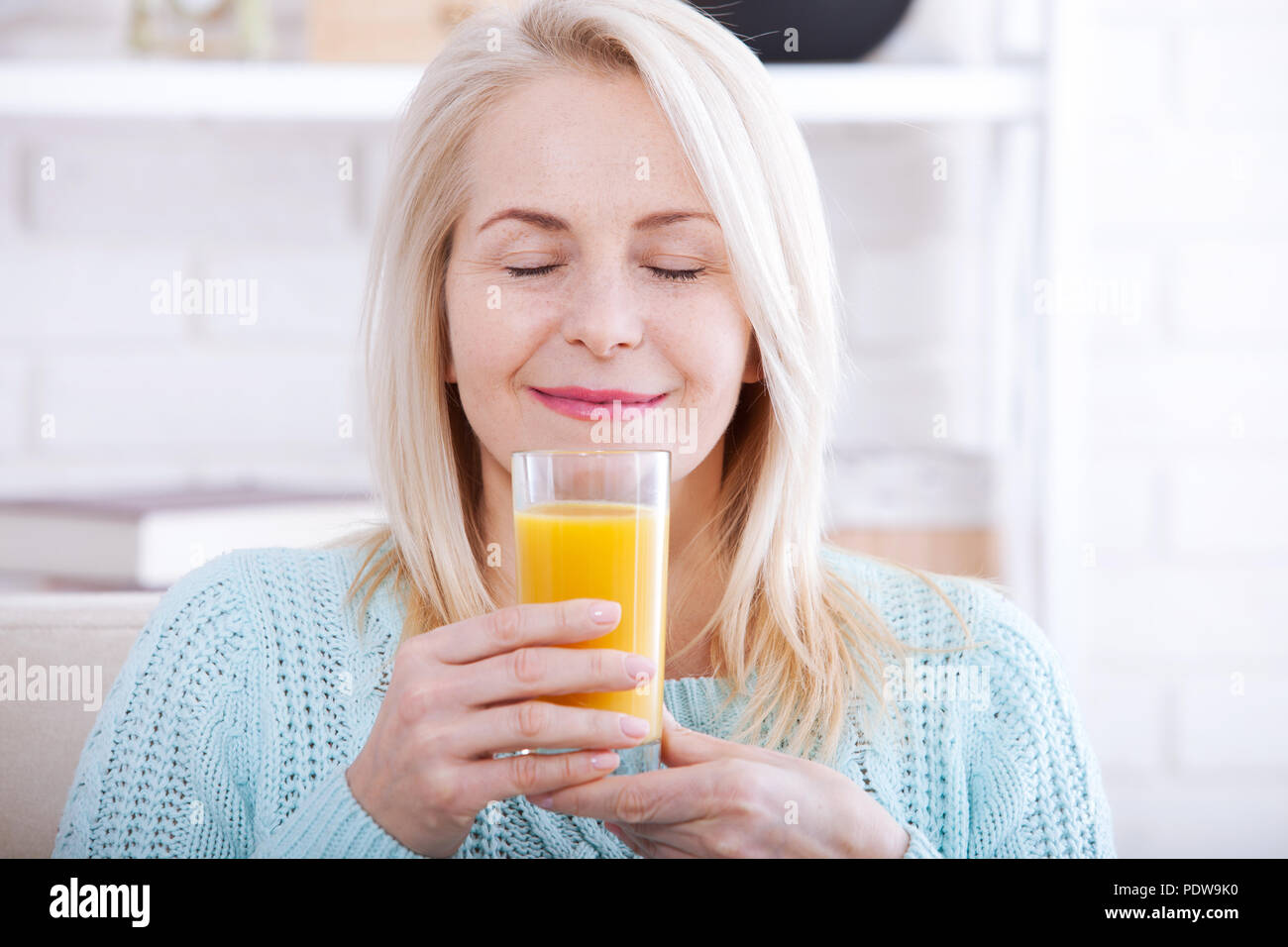 Smiling Woman drinking orange juice. Beau modèle de race blanche d'âge moyen à la maison. Banque D'Images