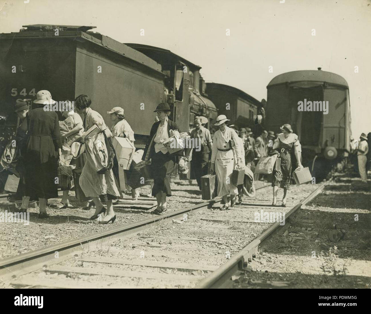 256 1 251348 StateLibQld femmes chargés de colis et de cas, laissant un train via les voies Banque D'Images