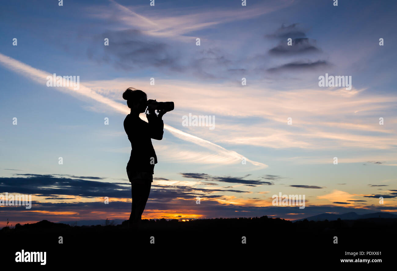 Une fille silhouetted against a sunset sky, prendre une photo avec un reflex numérique. Banque D'Images