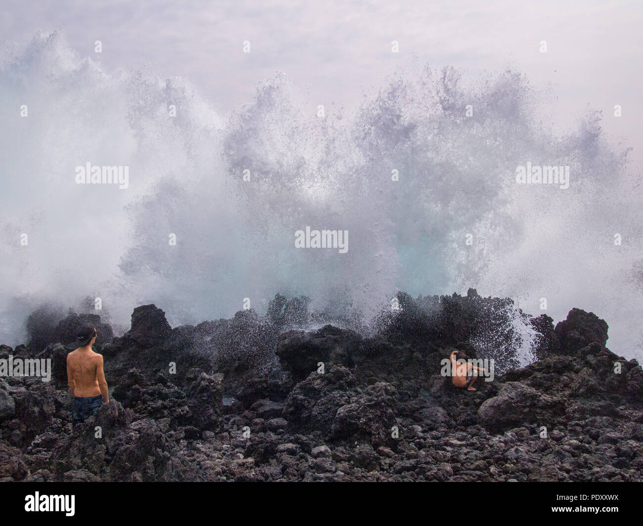 Deux adolescents se cacher derrière des roches de lave de vagues déferlantes, Hawaii, USA Banque D'Images