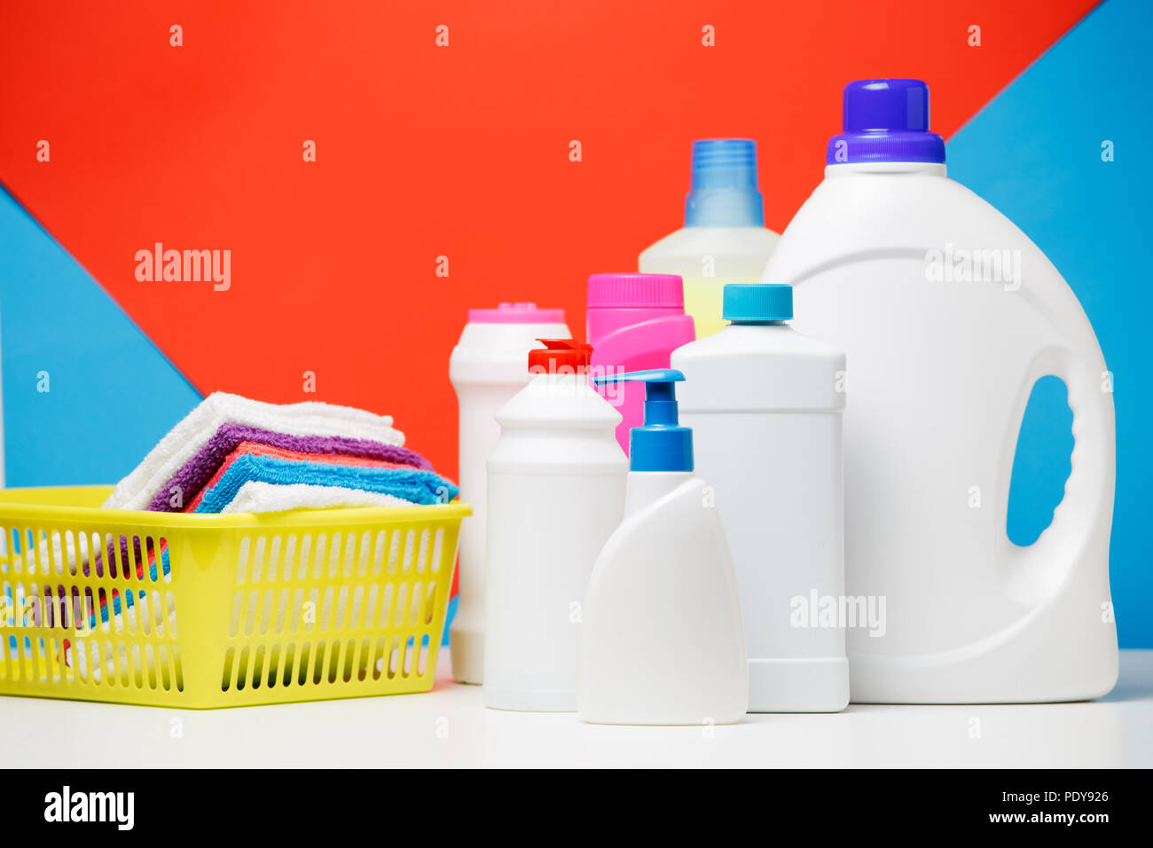 Photo de différentes bouteilles de produits de nettoyage et des serviettes colorées dans panier isolé sur fond bleu, rouge, lieu d'inscription Banque D'Images