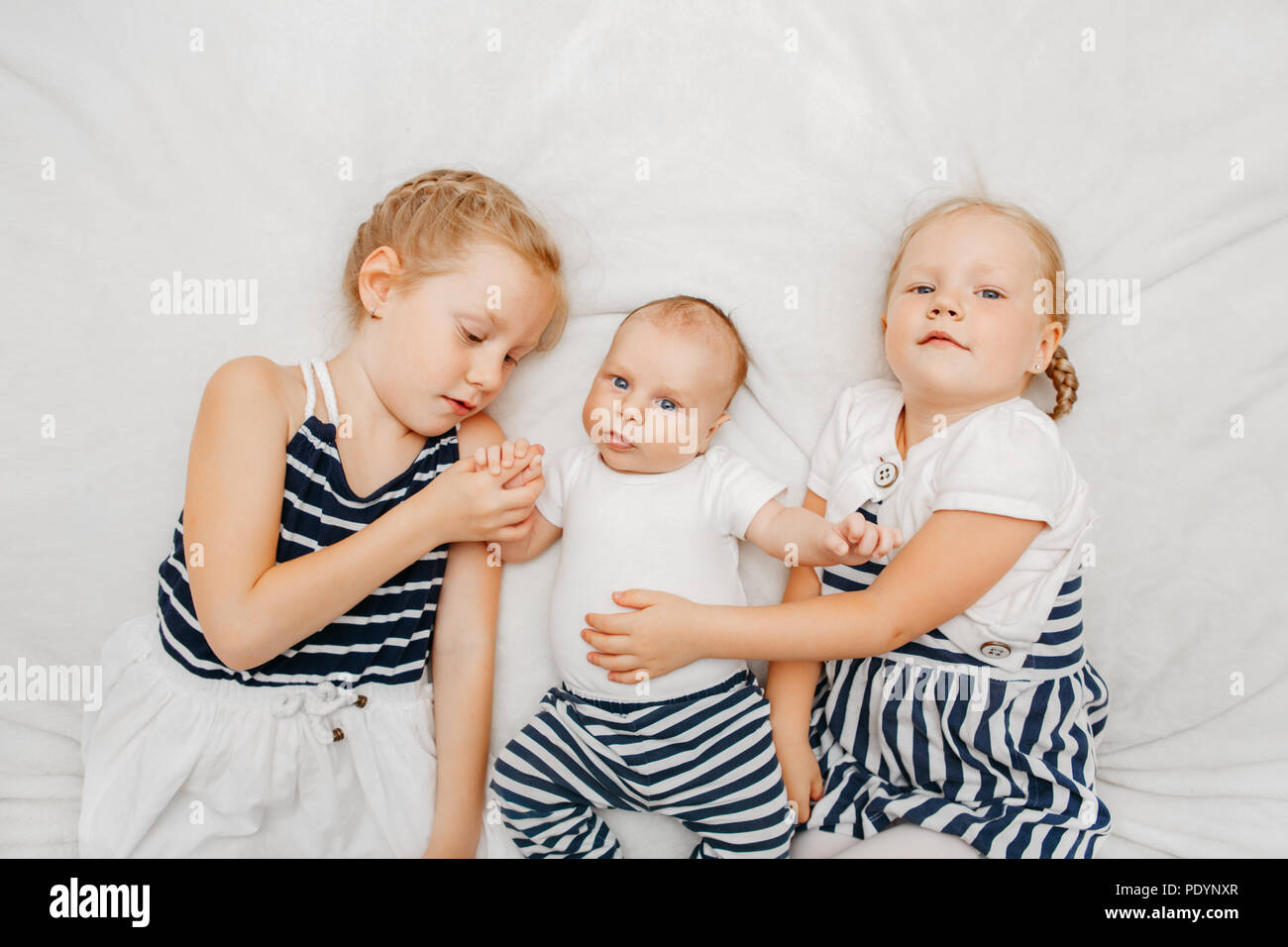 Vie Portrait Of Cute White Caucasian Girls Sisters Holding Petit Bebe Allonge Sur Une Couverture De Lit A L Interieur Les Freres Et Sœurs Plus Ages Avec Les Plus Jeunes Frere Sœur Photo