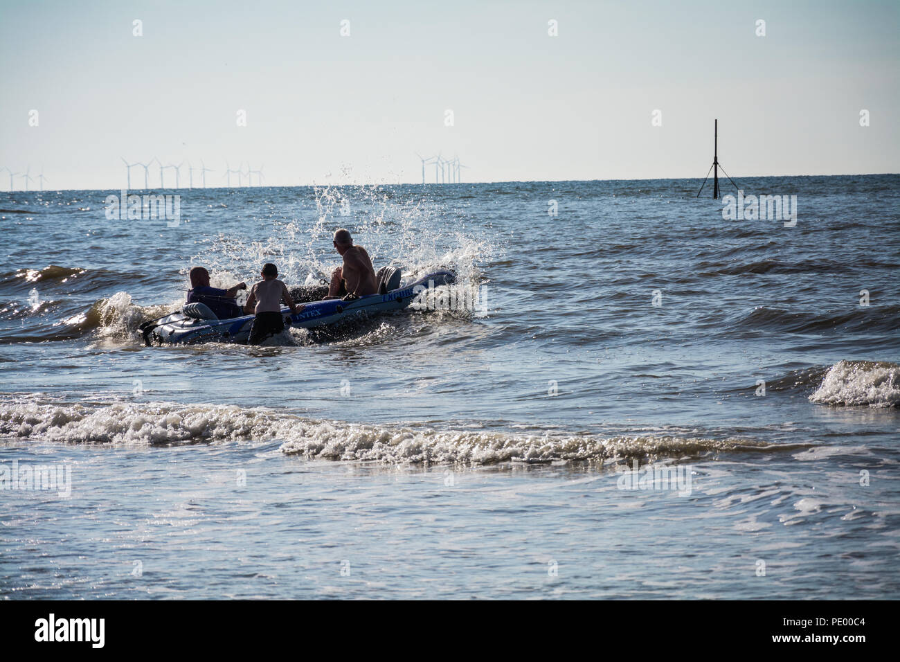 Touristes sur un canot gonflable jouant dans la mer pendant la canicule estivale de 2018. Parc éolien offshore à l'horizon. Prestatyn, pays de Galles du Nord, Royaume-Uni. Banque D'Images
