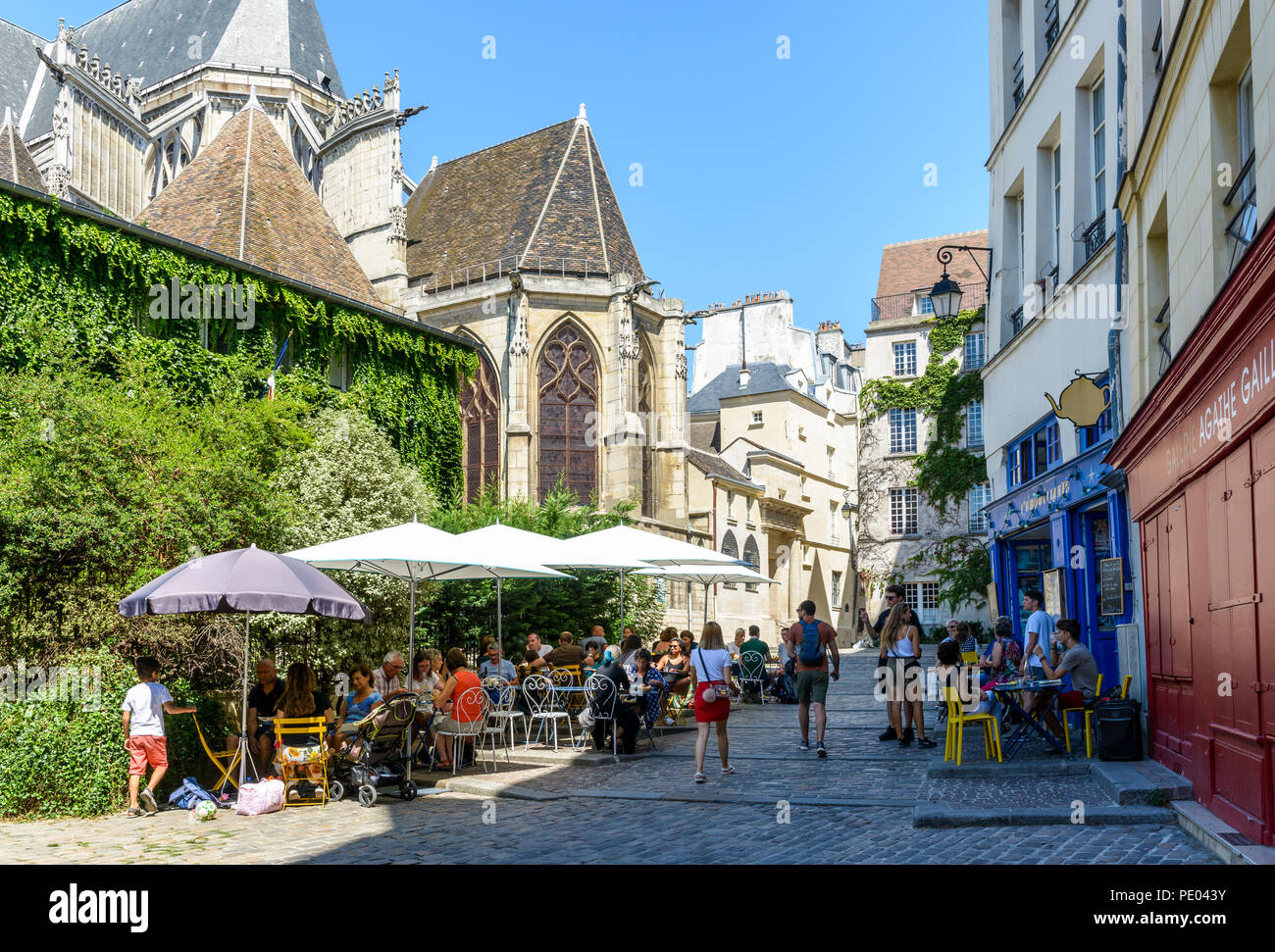 Une zone piétonne pavée située à Paris, en France, derrière l'église Saint-Gervais, avec des gens en train de déjeuner sur la terrasse d'un restaurant par une journée ensoleillée. Banque D'Images