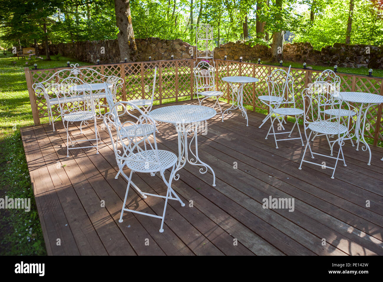 Chaises et tables blanches sur la plate-forme en bois. Terrasse verte dans un parc. Journée d'été. Banque D'Images