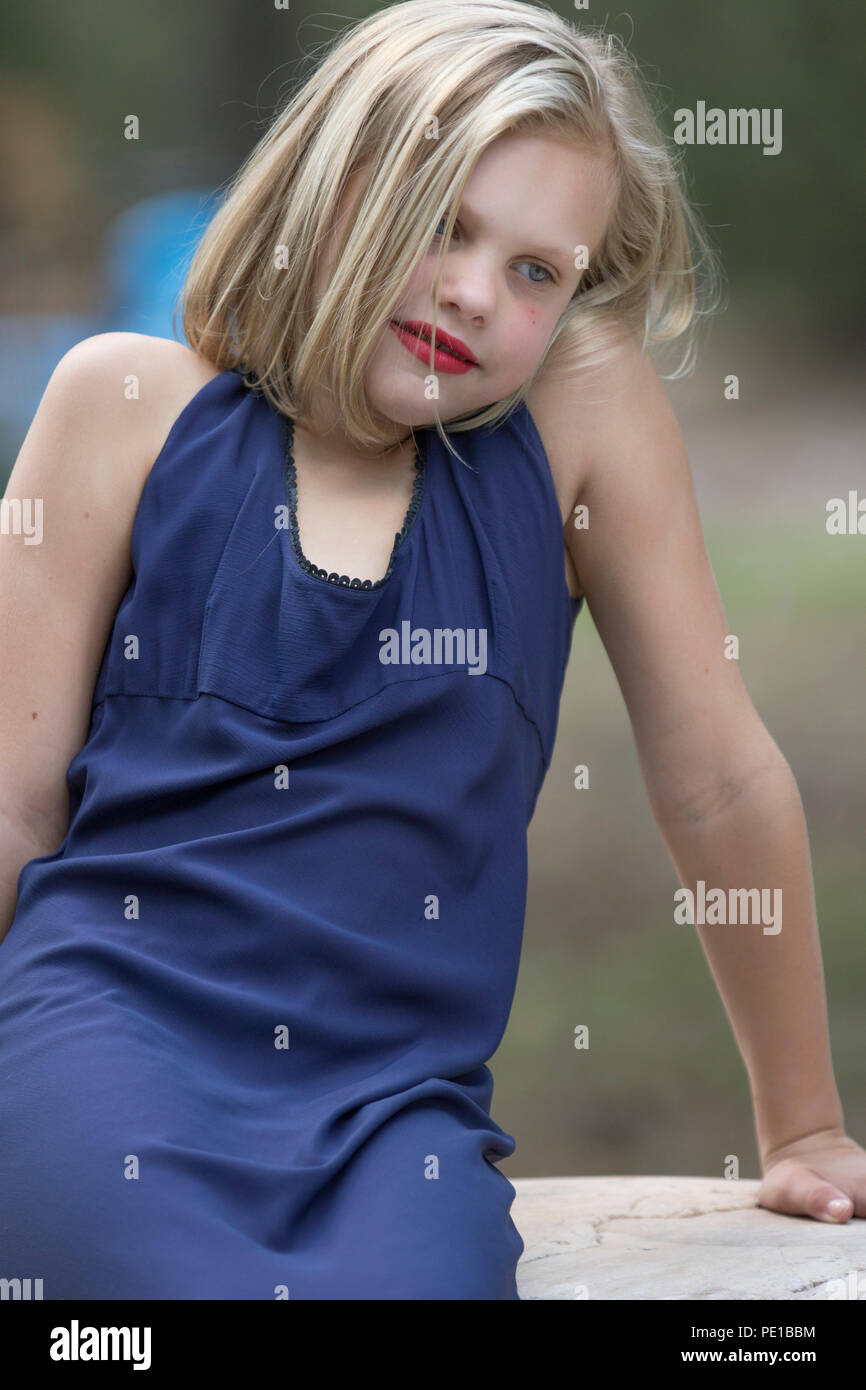 Jolie jeune femme blonde, des photos de mode , préadolescent. Assis sur un rocher, à l'extérieur, 3/4 profil, robe bleue, à la recherche en pleine réflexion, modèle publié. Banque D'Images