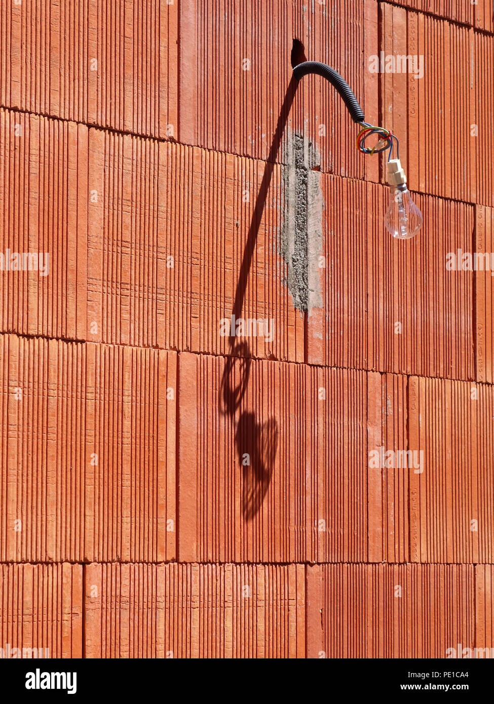 Ampoule unique suspendu à un fil à l'extérieur d'un mur récemment construit dans une maison de Cessenon-sur-Orb, France Banque D'Images
