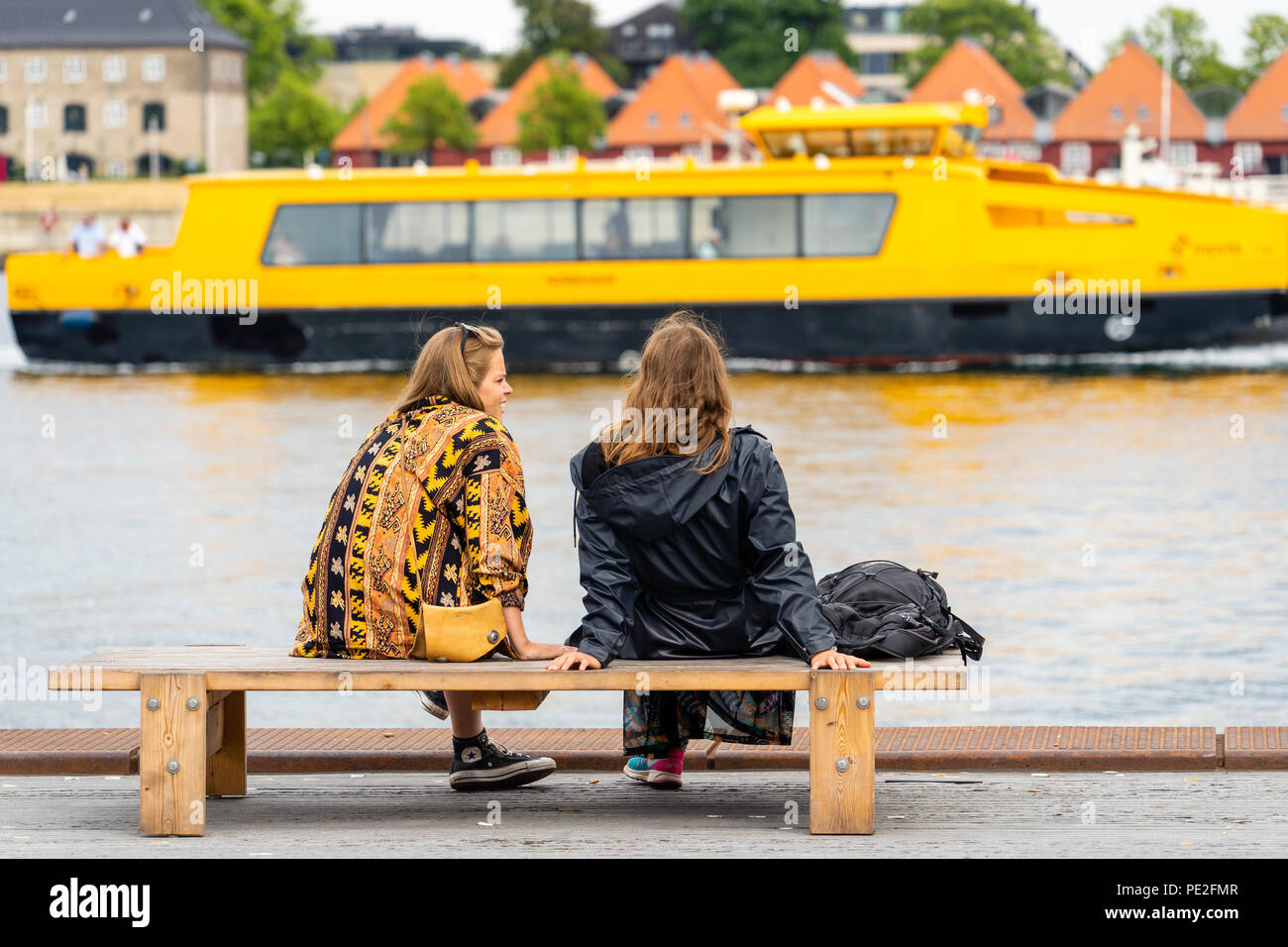 Deux jeunes femmes parlant sur banc Ofelia Square (Ofelia Plads) par le front de Copenhague, en passant par le bus de l'eau jaune Banque D'Images