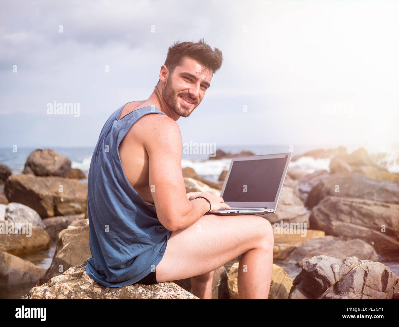 Young man working on laptop computer at beach Banque D'Images