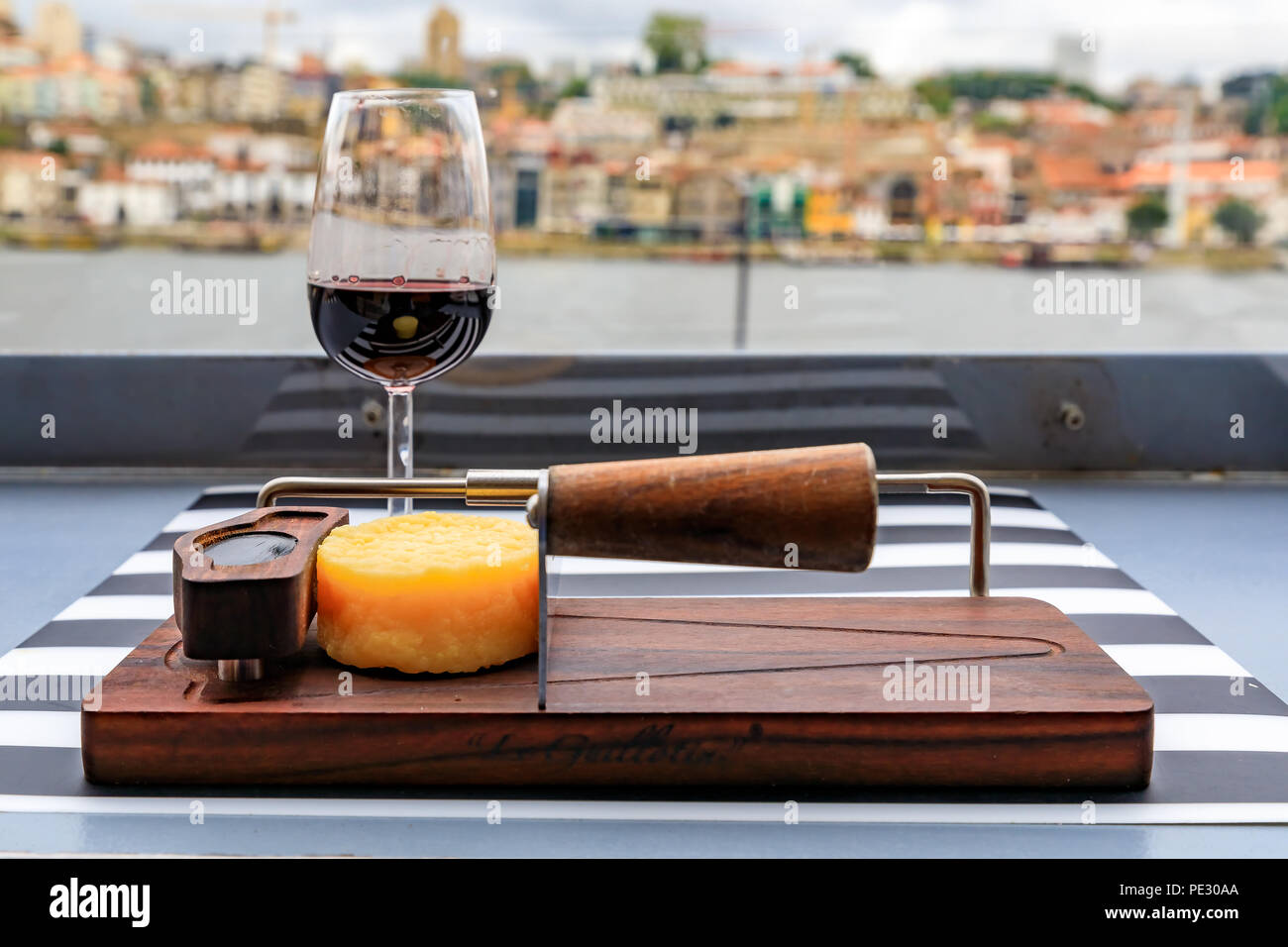 Verres de vin de porto et une petite roue de fromage sur le conseil à un restaurant en plein air avec le fleuve Douro et Le Pont Dom Luis I floues dans le backg Banque D'Images