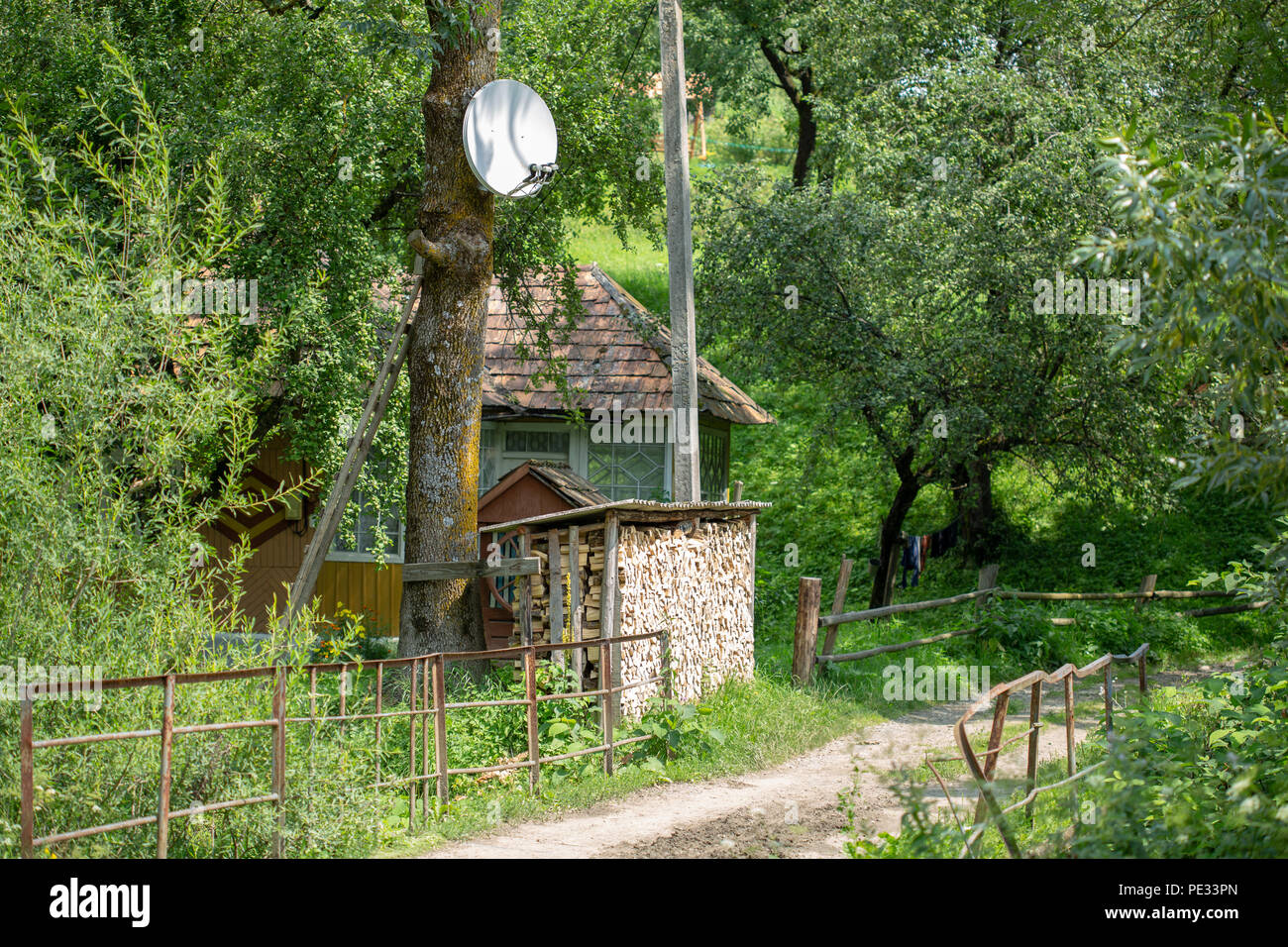 Partie d'une ancienne maison rurale avec une pile de bois de chauffage coupé et une antenne satellite. Banque D'Images