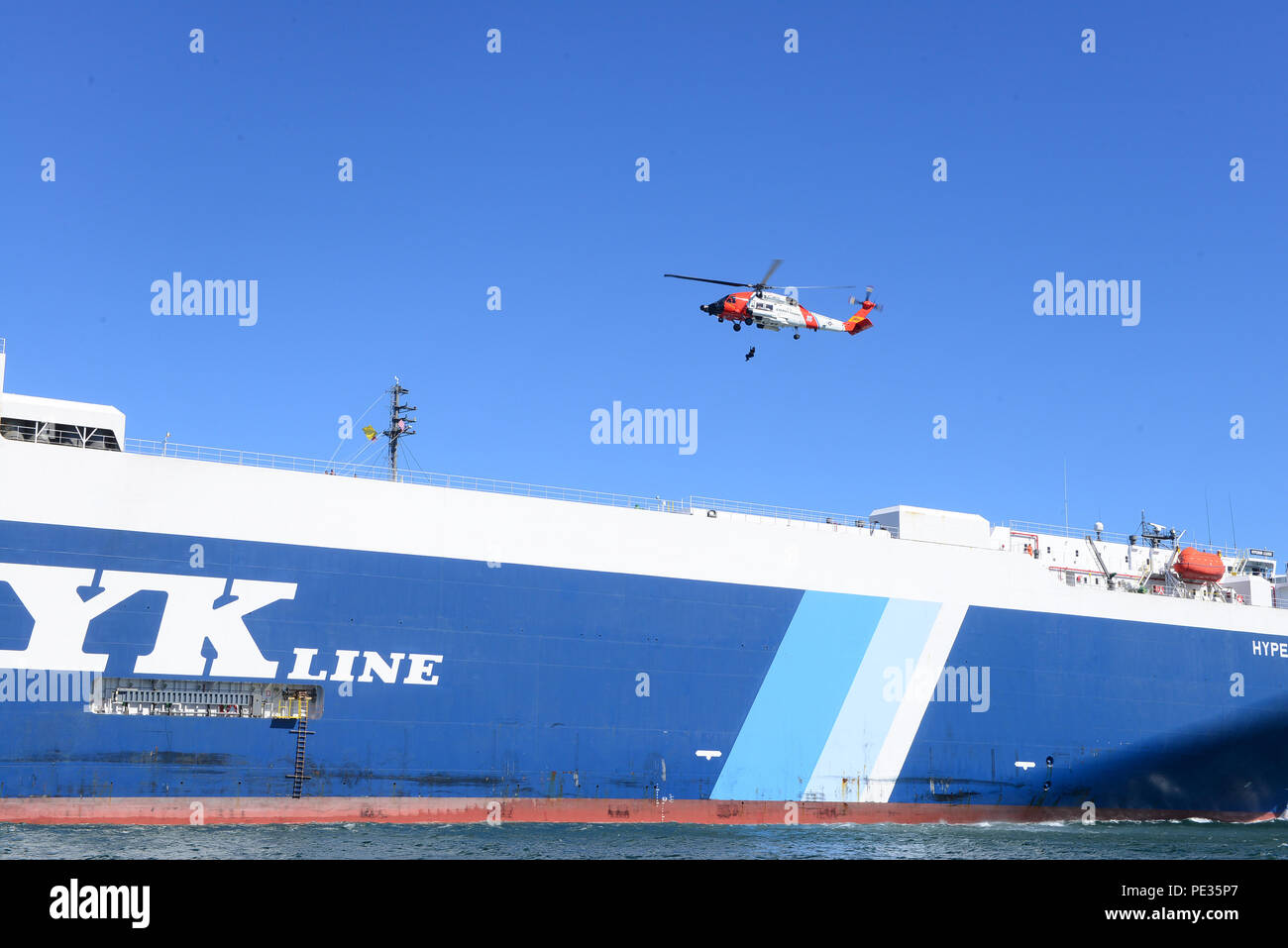 Un équipage d'hélicoptère Jayhawk MH-60 de la Garde côtière Air Station Astoria descend un membre de l'équipe d'arraisonnement du fleuve Columbia, du secteur privé dans l'hélicoptère après l'équipe a réalisé une pension de sécurité de la Leader Hyperion tandis qu'il est entré dans la rivière Columbia, de l'océan Pacifique, 9 septembre 2015. Les équipes d'embarquement conseil régulièrement les navires qui entrent aux États-Unis pour assurer la sûreté et la sécurité des ports américains. (U.S. Photo de la Garde côtière par Maître de 1re classe Levi Lire) Banque D'Images