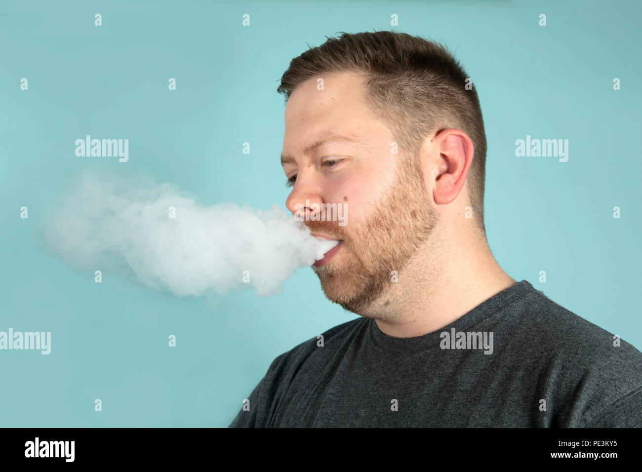 Jeune homme seine avec un nuage de fumée masquant son visage sur un fond gris en studio Banque D'Images