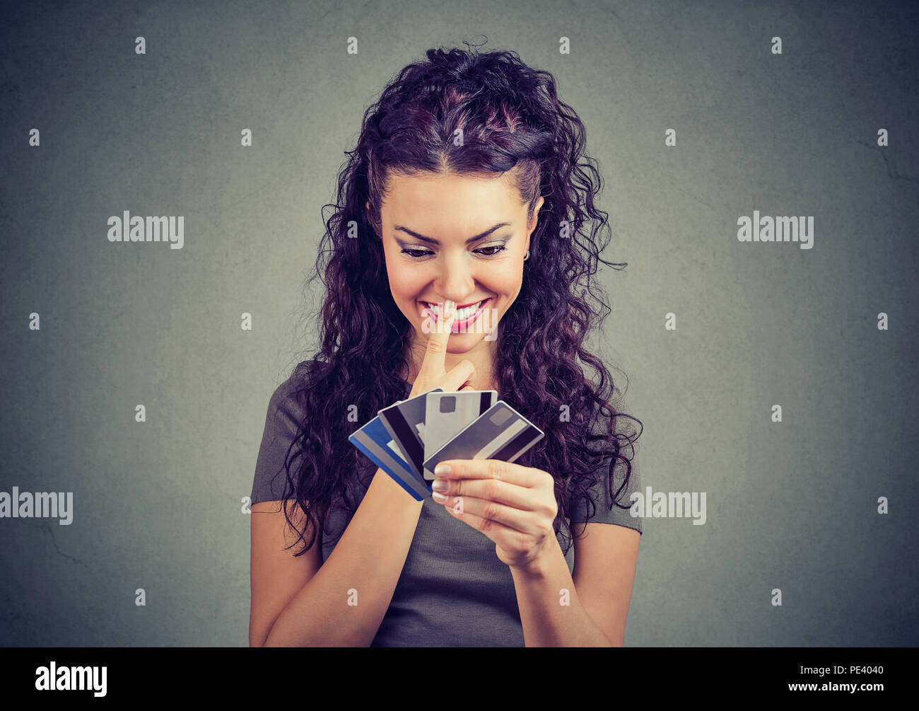 Charmante brunette holding pile de carte de crédit et de la réflexion sur les dépenses et shopping debout sur fond gris Banque D'Images